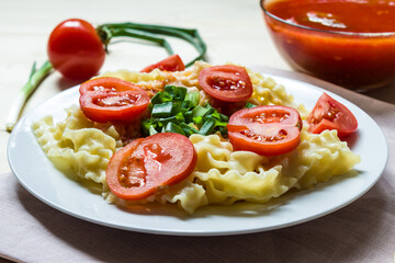 Pasta with fresh tomatoes and onions on a white plate.