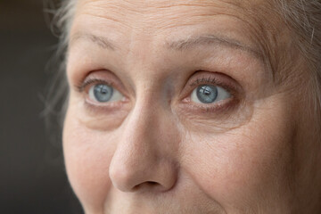 Blue eyes of thoughtful senior 70 woman looking away. Grey haired older lady upper face with...