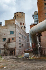 Old outdated Soviet cement plant. Metal grey tube in front, industrial building left. Obsolescent cement silo (tower) on backdrop. Temirtau, Kazakhstan.