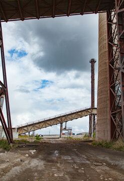 View on old outdated Soviet cement plant smoke stack and conveyor. Blue sky with clouds. Temirtau, Kazakhstan.