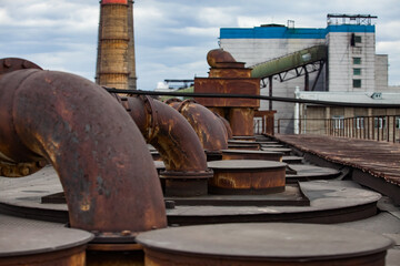 On the roof of heat electric plant. Old rusted pipes of ventilation system. Industrial building is out-of-focus. Blue sky with clouds. Karaganda, Kazakhstan.