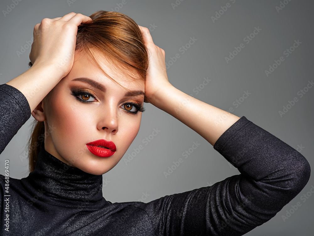 Wall mural Beautiful girl with red lips and short hair. Pretty face of an young sensual woman. Closeup portrait of a model with bright makeup on a face. Attractive female posing at studio  in black closes.