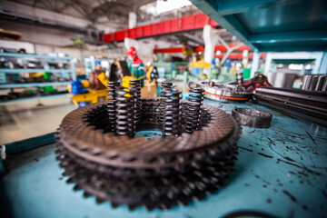 Truck-repairing plant. Close up photo of steel transmission part with spring. Low depth-of-field, partially blurred. Worker and interior is-out-of-focus.