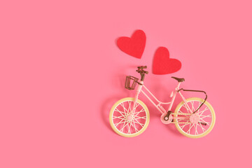 vintage toy bicycle and two red felt hearts pink background for congratulations on February 14,...