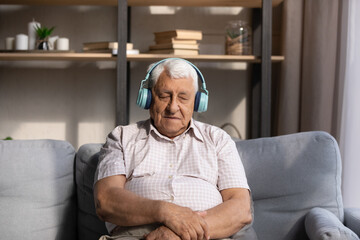 Tired calm old 80s man listening to music from bright big wireless headphones, relaxing, meditating with closed eyes, sleeping, recreating, reloading, enjoying lazy break, leisure time at home