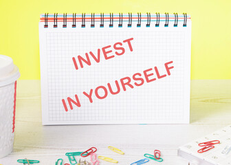 invest in yourself text on a notebook standing on a table on a yellow background