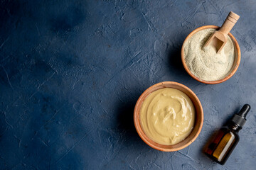 Cosmetic green clay in a wood bowl with aroma oil on a blue background. Natural cosmetic concept.