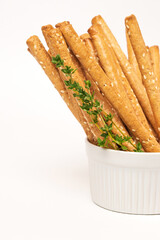 Classic crispy bread sticks grissini with thyme stems and sesame seeds in white form. Traditional Italian pastry breadsticks on white background with copy space