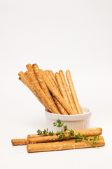Classic crispy bread sticks grissini with thyme stems and sesame seeds in white form. Traditional Italian pastry breadsticks on white background with copy space