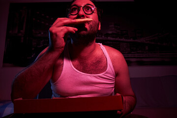 A 40-year-old unshaven overweight man watches TV, shows various emotions and eats pizza. lazy middle-aged man