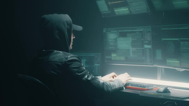 Hooded cybercriminal making cybercrime and hacking big data servers security system on computer in dark underground hideout