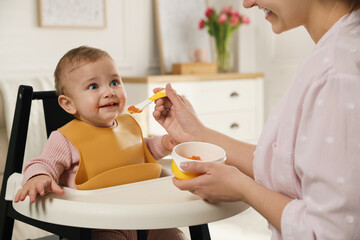 Mother feeding her little baby at home. Kid wearing silicone bib