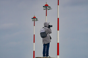 Man with camera taking planes who take off in airport area in background radar antennas