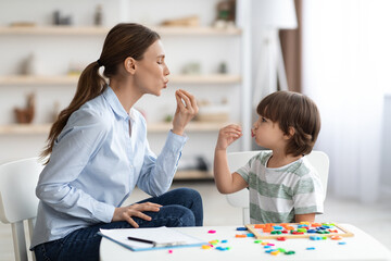 Young woman speech therapist studying together with small kid, learning practice pronunciation exercises with little boy