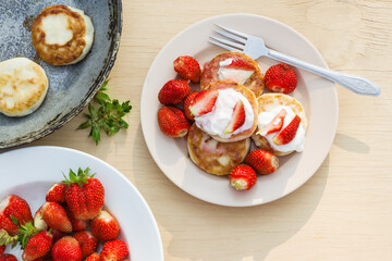 Cheesecakes with strawberries and sour cream. Breakfast in nature. Traditional Russian and Ukrainian dish.