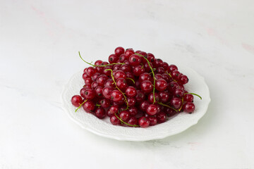 Red currant on a white plate on a white background