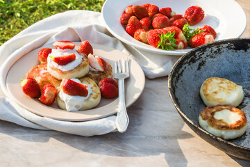 Cheesecakes with strawberries and sour cream. Breakfast in nature. Traditional Russian and Ukrainian dish.