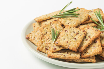 Square diet cookies with rosemary, flax seeds and spices  in a light plate on white background. Crunchy herbal crackers close up plan with low depth of field
