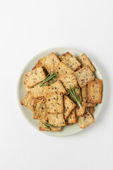 Square diet cookies with rosemary, flax seeds and spices  in a light plate on white background. Crunchy herbal crackers top view