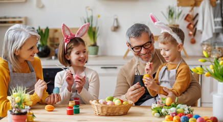 Happy little children creating beautiful painted eggs for Easter with loving senior grandparents
