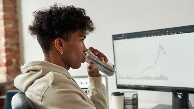 Portrait focused african american trader drinking energy drink near screens with data index chart stock market
