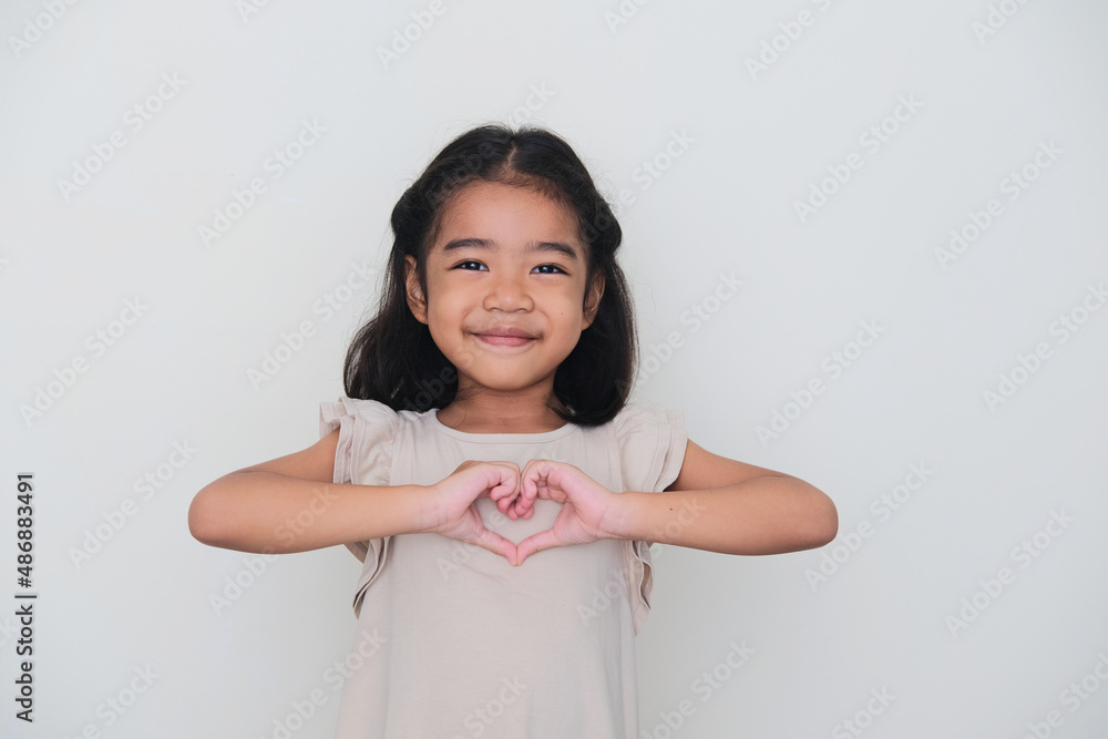 Wall mural Asian kid smiling with her hand making heart shape on chest - Wall murals
