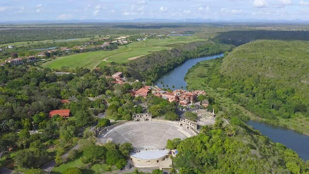 Cinematic drone shot of old historic Amphitheater and Altos De Chavon on mountaintop with scenic landscape and river in backdrop