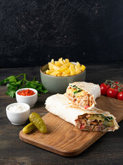 Delicious shawarma sandwich on wooden background with french fries and pickles. Vertical