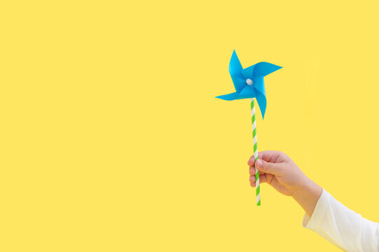 Child holding paper windmill on yellow background