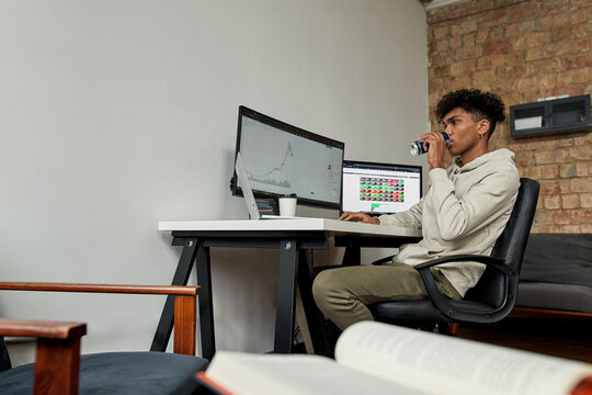 Portrait focused african american trader drinking energy drink near screens with data index chart stock market