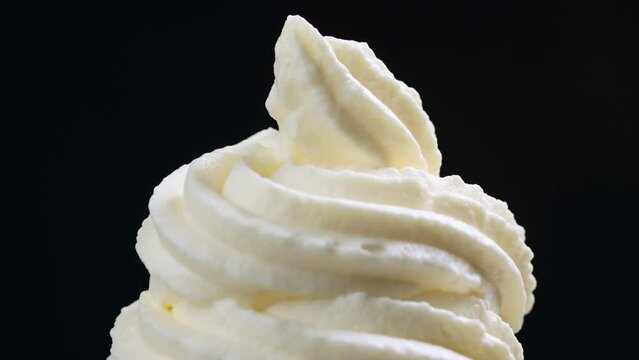 close up of rotating whipped cream on black background, the cook squeezes the cream from the decorating bag 