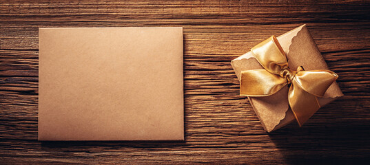 Kraft paper gift box with gold ribbon bow and envelope on old wood texture