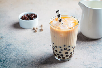Milk bubble tea with tapioca pearls in glass, gray background.