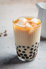 Milk bubble tea with tapioca pearls in glass, gray background.
