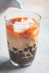 Milk bubble tea with tapioca pearls in glass, gray background.