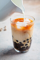 Milk bubble tea with tapioca pearls in glass, gray background.