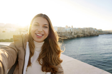 Charming woman making selfie photo in Polignano a mare town on sunset, Apulia, Italy