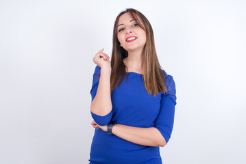 Fototapeta premium Cheerful Young arab woman wearing blue dress over white backgtound with hand near face. Looking with glad expression at the camera after listening to good news. Confidence.