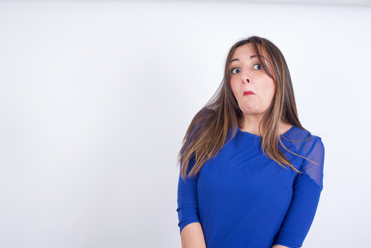 Young arab woman wearing blue dress over white backgtound with snobbish expression curving lips and raising eyebrows, looking with doubtful and skeptical expression, suspect and doubt.