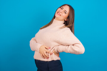 Young arab woman wearing knitted sweater over blue backgtound  got back pain
