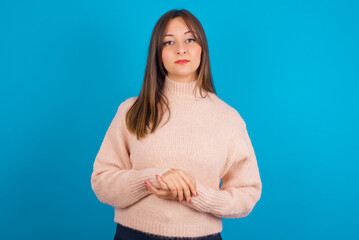 Photo of cheerful confident Young arab woman wearing knitted sweater over blue backgtound  arms together