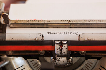 The German word tax declaration written with an old mechanical typewriter with red and black ribbon in black color on a white sheet of paper