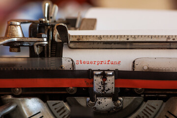 The German word tax audit written in red ink on a white sheet of paper with an old mechanical typewriter with red and black ink ribbon