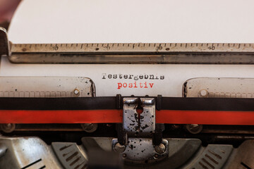 The German word test result positive written with an old mechanical typewriter with red and black ribbon in black and red color on a white sheet of paper