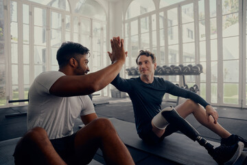 Two friends training in the gym - one with a prosthesis . Two men high fiving in the gym after a...