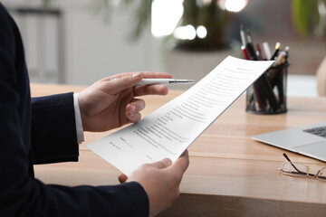 Man reading document at table in office, closeup. Signing contract - obrazy, fototapety, plakaty