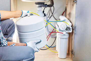 Plumber hand in gloves replace water filter cartridges at home kitchen. Fix purification osmosis...