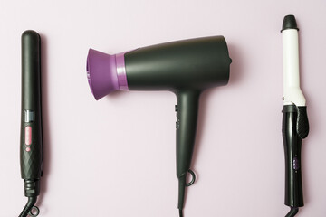 professional hairdresser set, hair dryer, curling iron, straightener in black on purple background