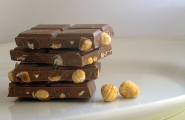 Chocolate and hazelnuts. Pieces of chocolate with hazelnuts on a white plate.