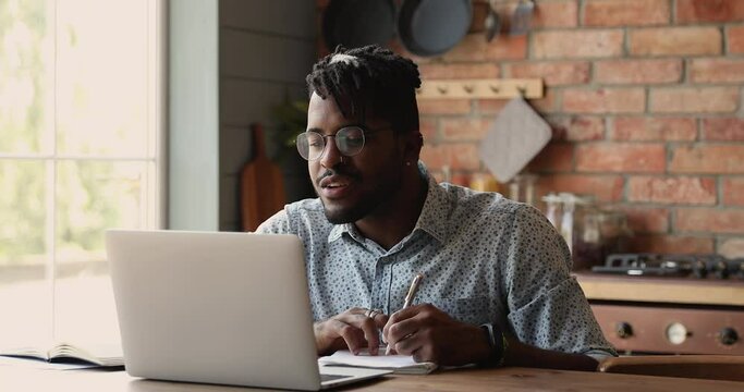 Black Man Remote Student Watch Web Training Class Webinar On Laptop Online Study New Information Make Brief Notes. Young Hipster Guy Sit By Pc At Home Kitchen Improve Professional Skills Via Elearning